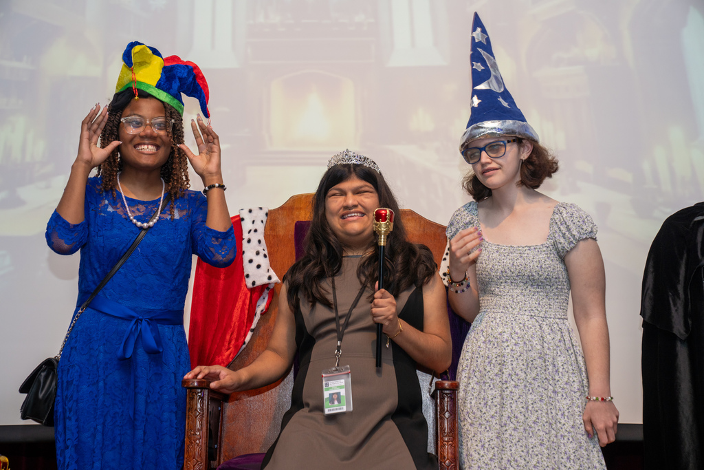 A group of friends are wearing hats and being silly for a photo on stage in the music building. 
