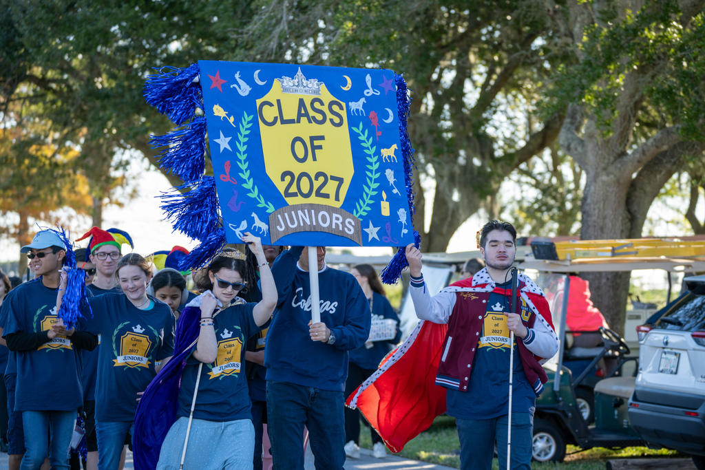 Students hold  a big blue sign that says "Class of 2027, Juniors" walk through the streets of FSDB.