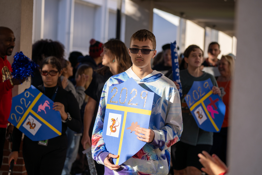 A student is holding a shield sign that says "2029" walking through the parade. 