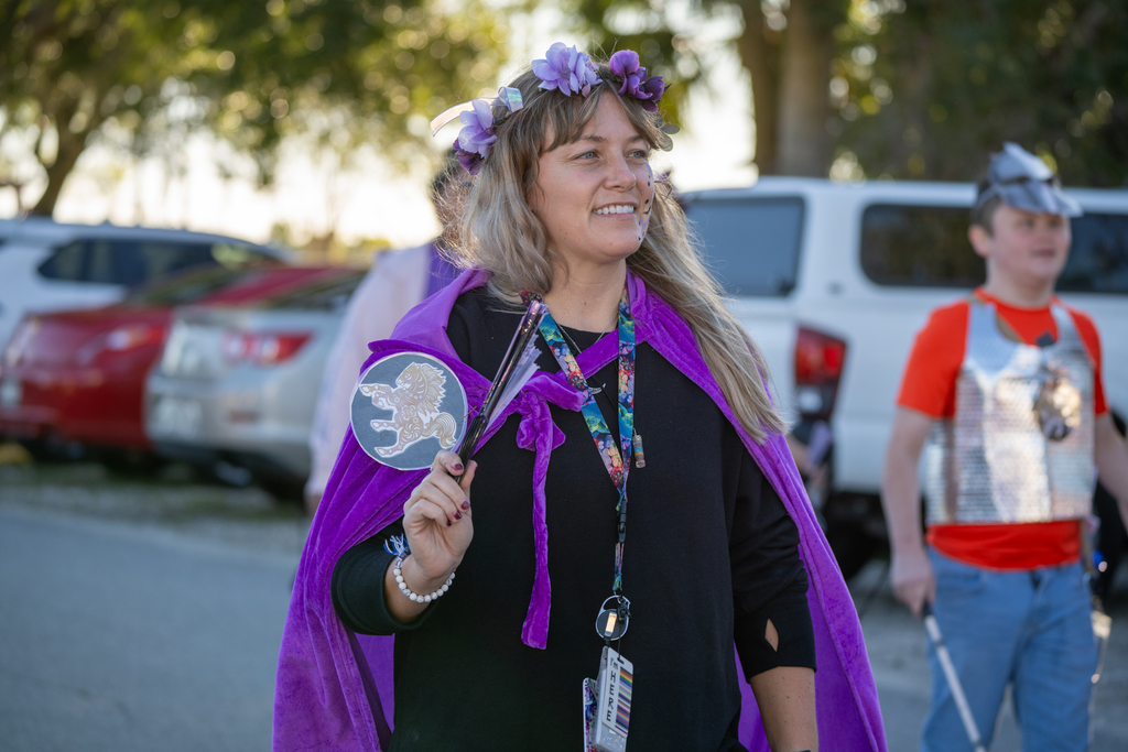 A staff member is wearing black and purple clothing smiling as she walks through the streets of FSDB. 