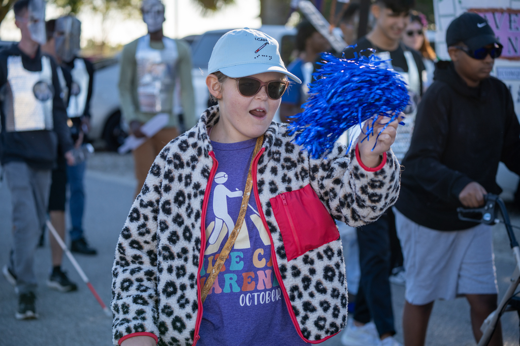 A student is waving a blue pom pom walking down the streets of FSDB for the parade. 