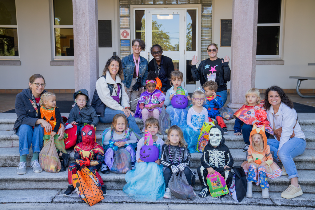ELC students and staff dressed up in Halloween costumes smile for a photo on the stairs of Moore Hall. 