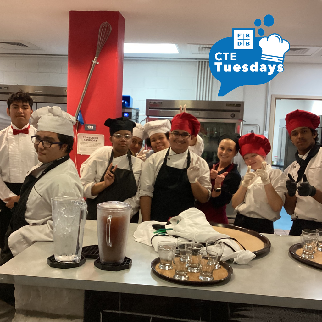 Photo of Culinary Arts student wearing red and white chef hat and aprons pose for a photo inside the Dragons Lair kitchen. 
