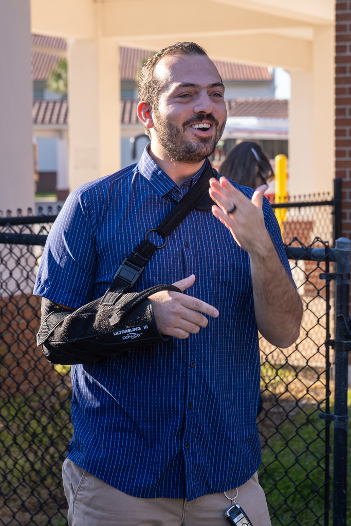 Zachary with a surprised look on his face signing "thank you", he's wearing a blue button down shirt and khaki pants.