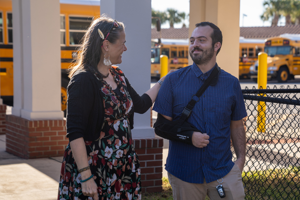 Tracie Snow looking at Zachary as they are walking.  They both have big smiles on their faces. Tracie Snow has her hair pinned back on one side and is wearing a black cardigan with a black, burgundy, white and green dress.