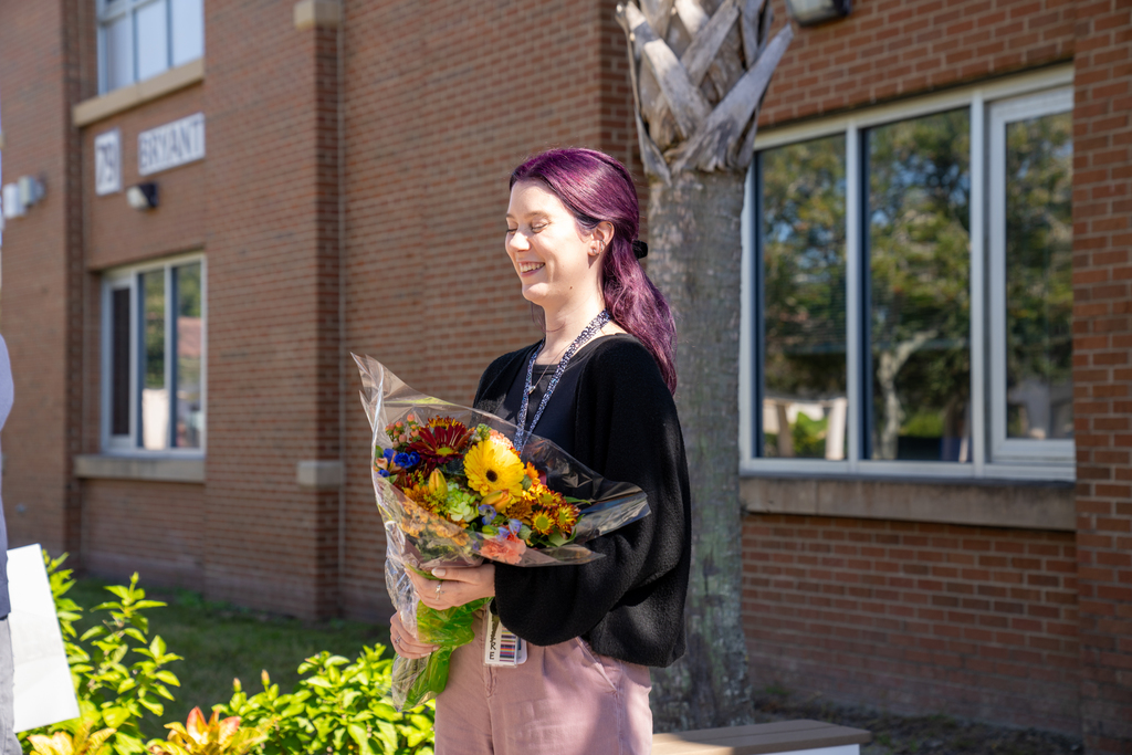 Sde view of Hannah and she's holding a bouquet of flowers. The flowers are yellow, orange, dark red and green. 
