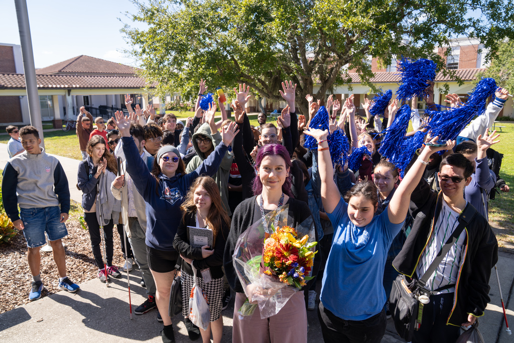 Hannah standing in front and the Blind High School students behind her cheering.  Some have blue pom-poms and some students have their hands in the air. 