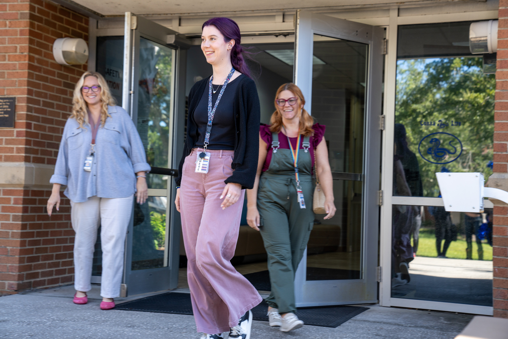 Hannah walking out of Bryant Hall with a very surprised look on her face.  She is wearing pink pants, with a dark navy or black shirt and a black sweater. Her dark purple hair is pulled back with a clip in a "half pony".