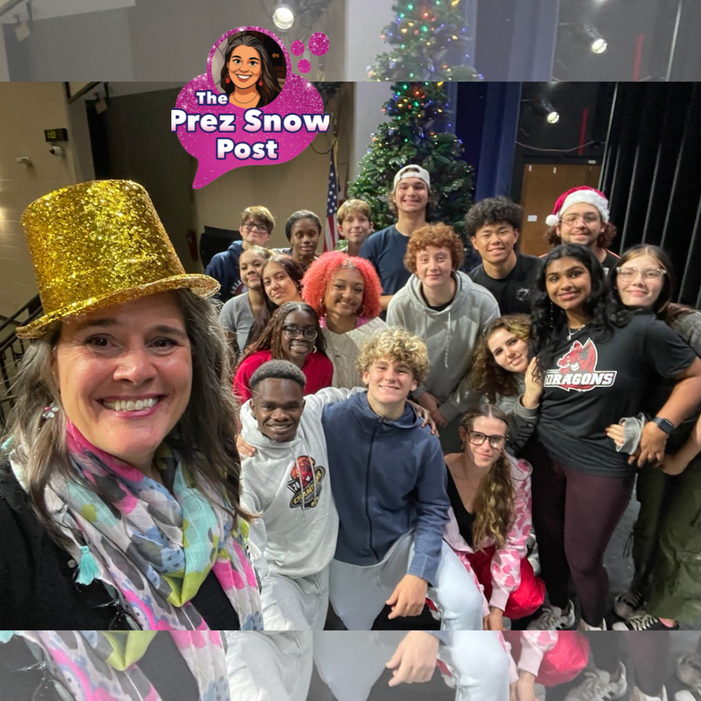 Tracie Snow wearing a yellow sparkle hat taking a selfie with the Dance Troupe on stage in Kirk. 