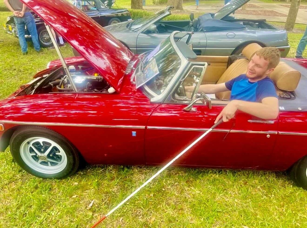 A FSDB Alumni is sitting in a red vintage car parked on the FSDB campus in Palm Row.