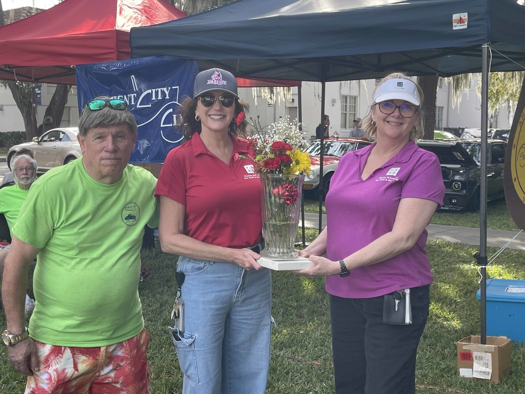 Two FSDB staff members hold a bouquet of flowers smiling next to a visitor on the FSDB campus in Palm Row.