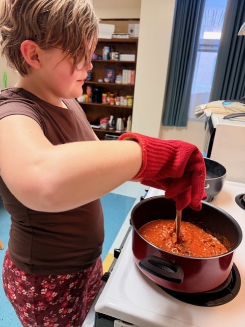 Maddie wearing gloves and stirring the food in the pot in the kitchen. 