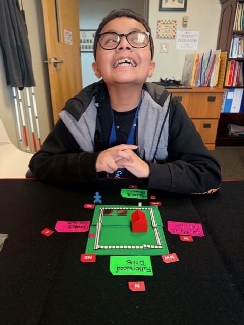 Manny is smiling for a photo with his tactile map inside the office. 