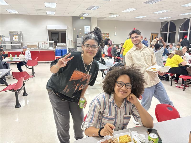 Three students pose for their photo while holding their thanksgiving meal inside the cafeteria.
