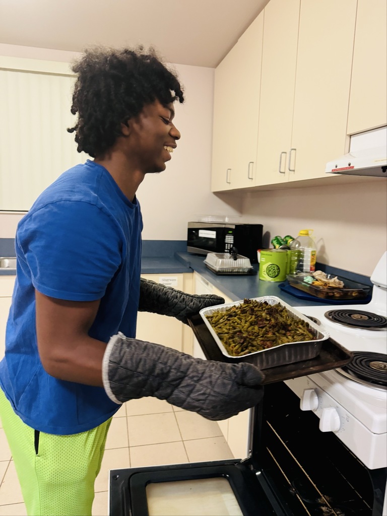 A student is wearing black oven mitts taking out the green bean casserole out of the oven.