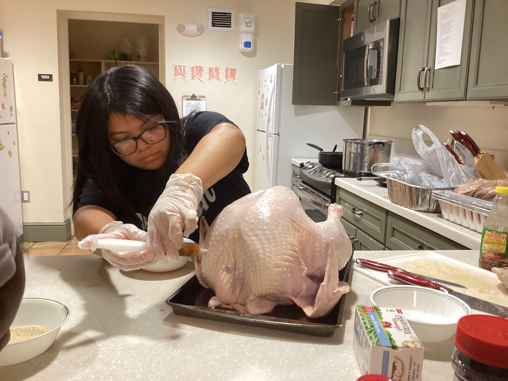 A student is injecting the turkey with flavor inside the apartment kitchen.