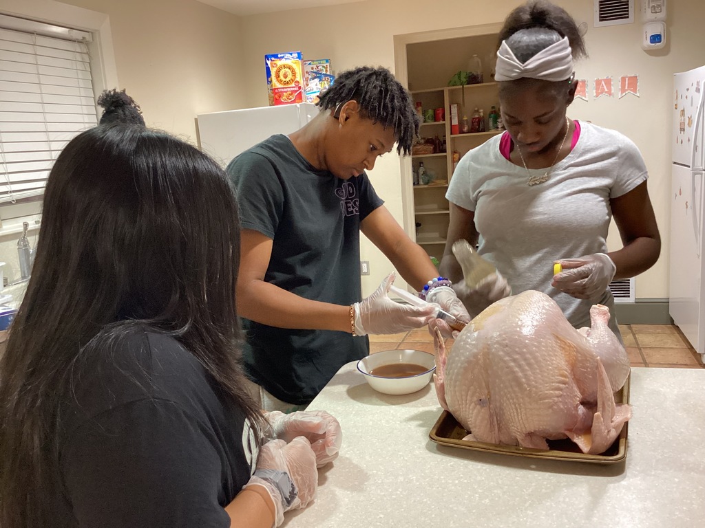 Apartment girls work on injecting the turkey together inside the apartment kitchen.