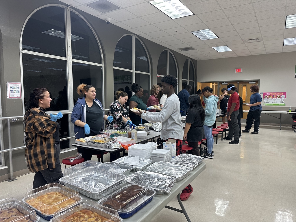 Staff members stand helping students scoop their meals onto plates inside the kitchen.