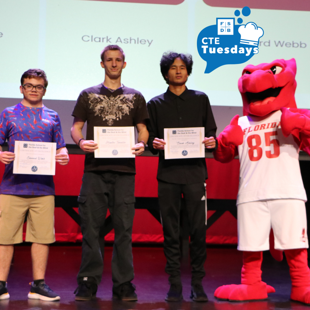 Students who won a CTE award stand on stage in Kirk holding their certificate and smiling with Samy the Dragon.