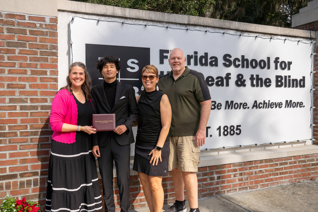 Clark smiles with his parents and President Tracie Snow by the FSDB sign.