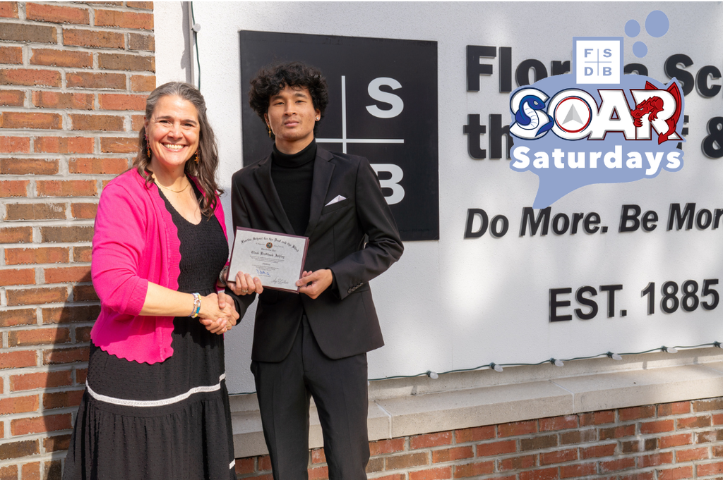 Clark and President Tracie Snow handshake together as Clark holds his diploma by the FSDB sign.