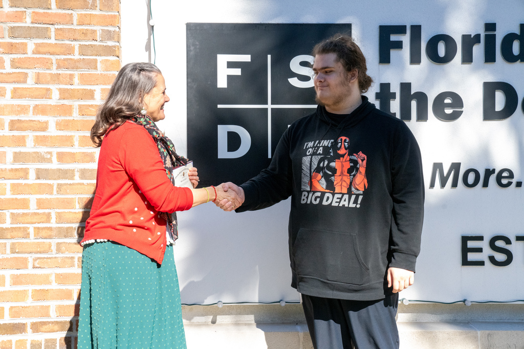 Tracie Snow handshakes Shane by the FSDB sign. 