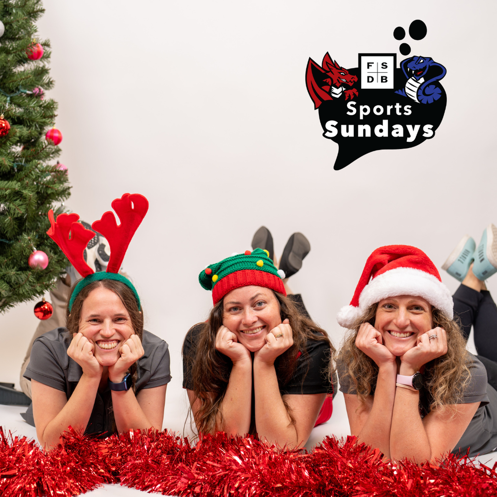 Three FSDB Athletic Staff wearing Christmas headwear laying on the floor with red tinsel in front of them with a Christmas tree in the back. 