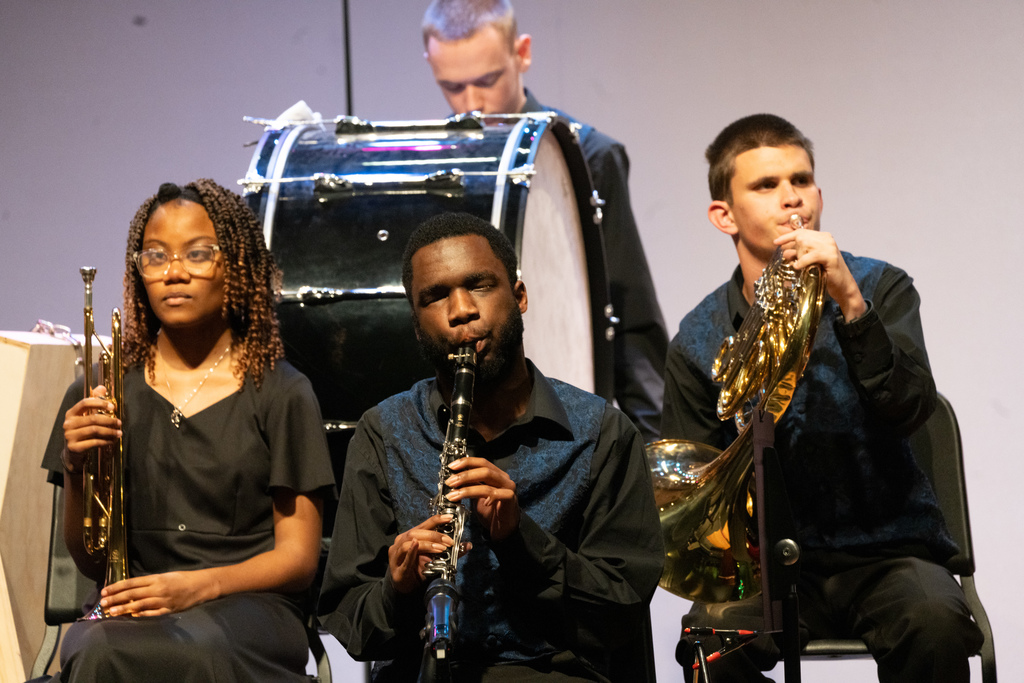 Three band students playing instruments on stage in the Music building.