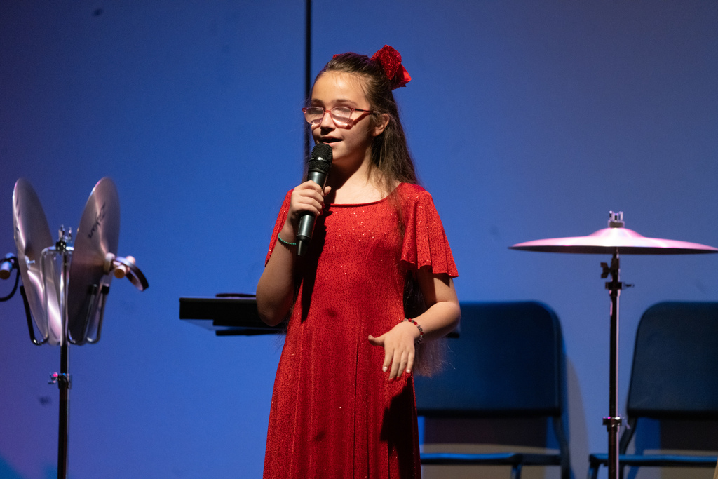 A blind elementary school student wearing a red dress sing on stage in the Music building.