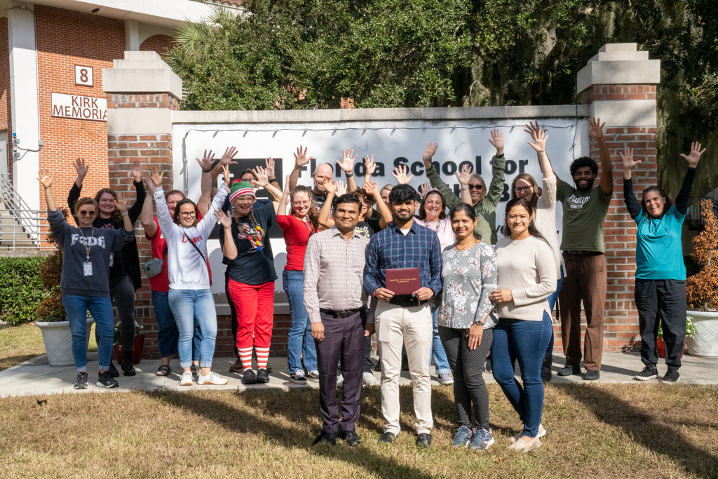 Sujal smiles with his family in front of staff members cheering in the background by the FSDB sign. 