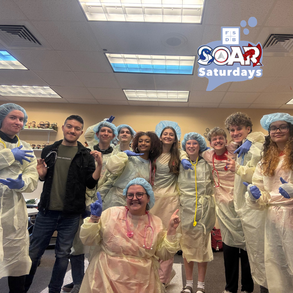 Group of students dressed in PPE and gloves smile for a photo together inside the classroom. 