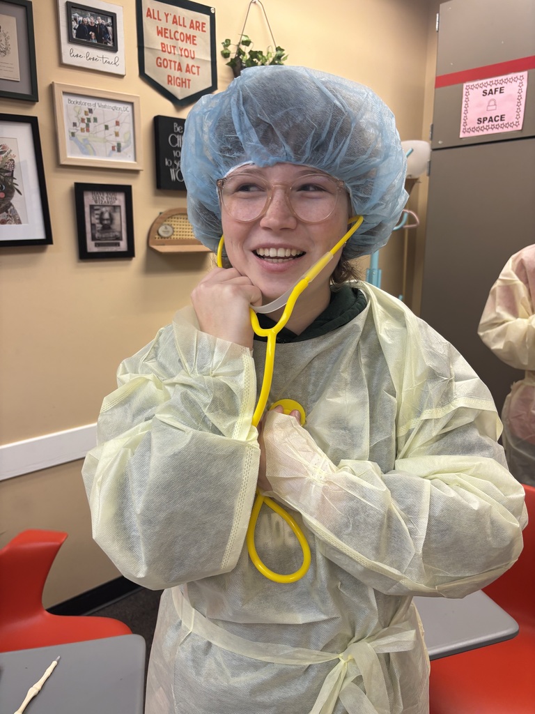 A student dressed in PPE holding a stethoscope inside the classroom. 