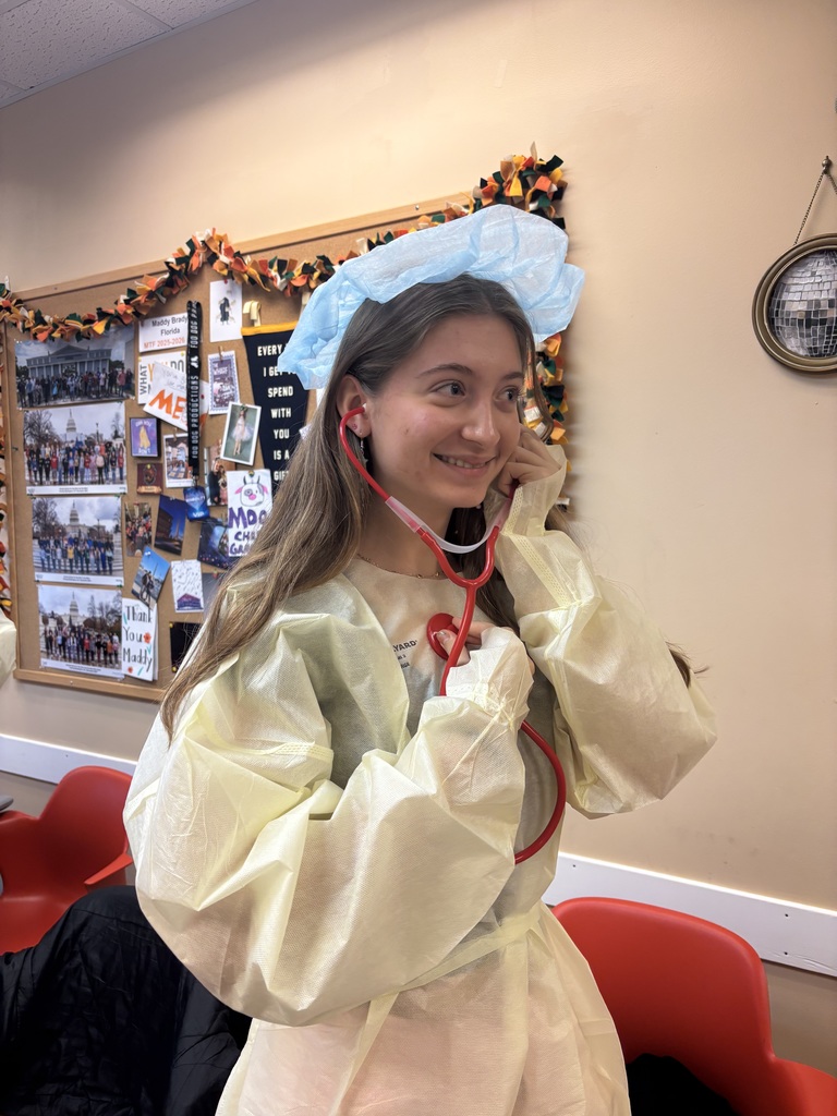 A student dressed in PPE and holding a stethoscope to her ears inside the classroom. 