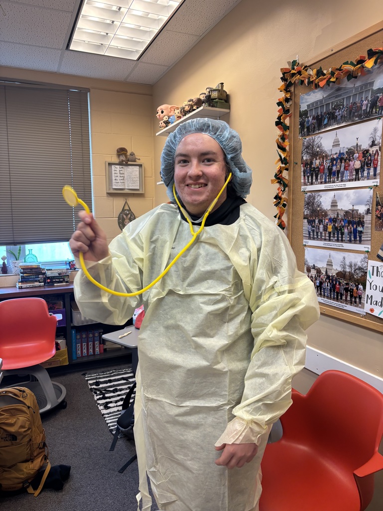 A student dressed in PPE holding a stethoscope inside the classroom. 