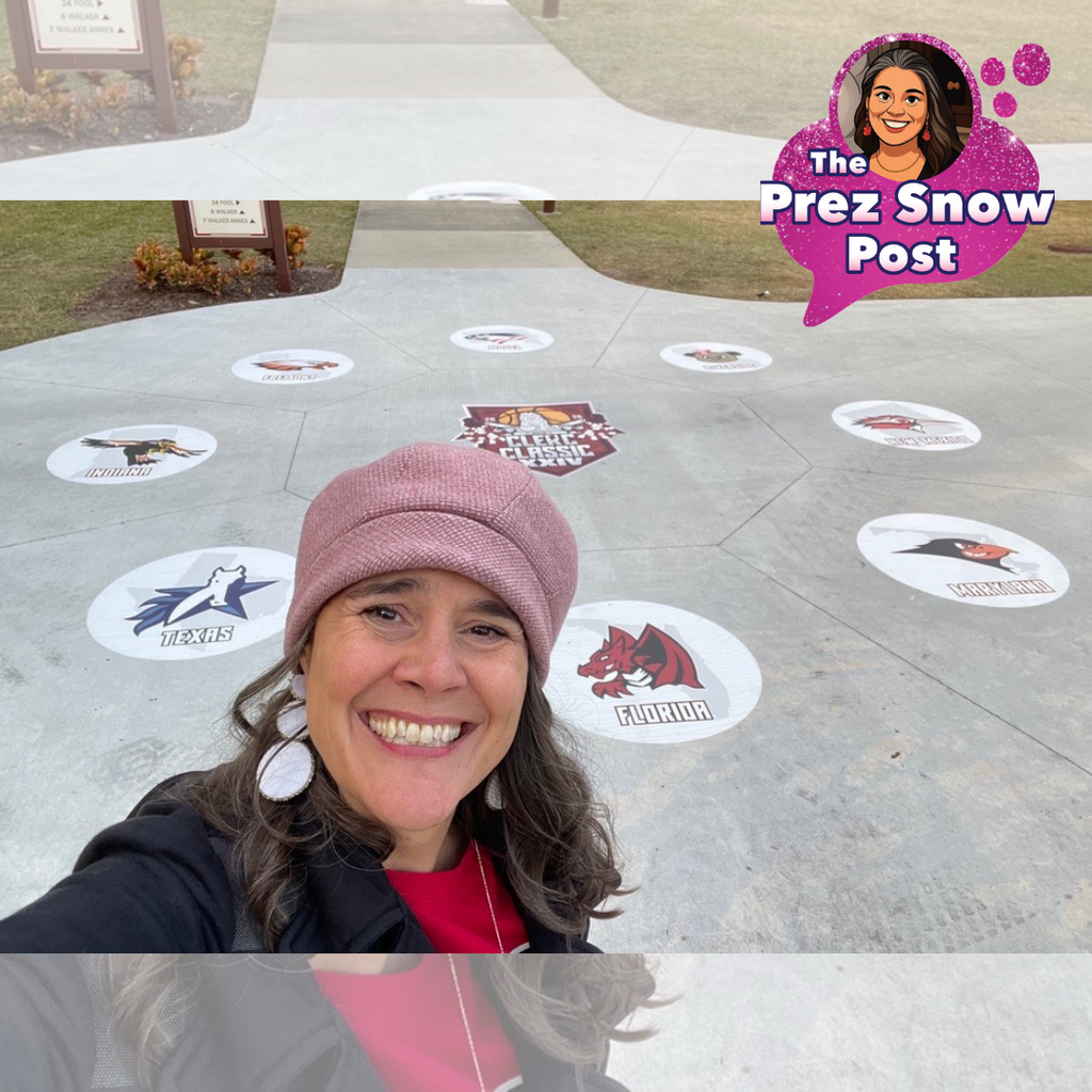 Happy President Selfie standing in front of the new sidewalk decals welcoming visitors to the campus. (President Snow is smiling brightly wearing a pink hat and black jacket because yes, it is COLD in Florida). Photo shows an outdoor sidewalk area with circular decals featuring various team logos and names arranged in a circular pattern on the concrete surface. At the center is a larger decal that reads “Clerc Classic XXIV” with a graphic design. Surrounding it are smaller decals representing different states and mascots of the teams playing in the tournament.
