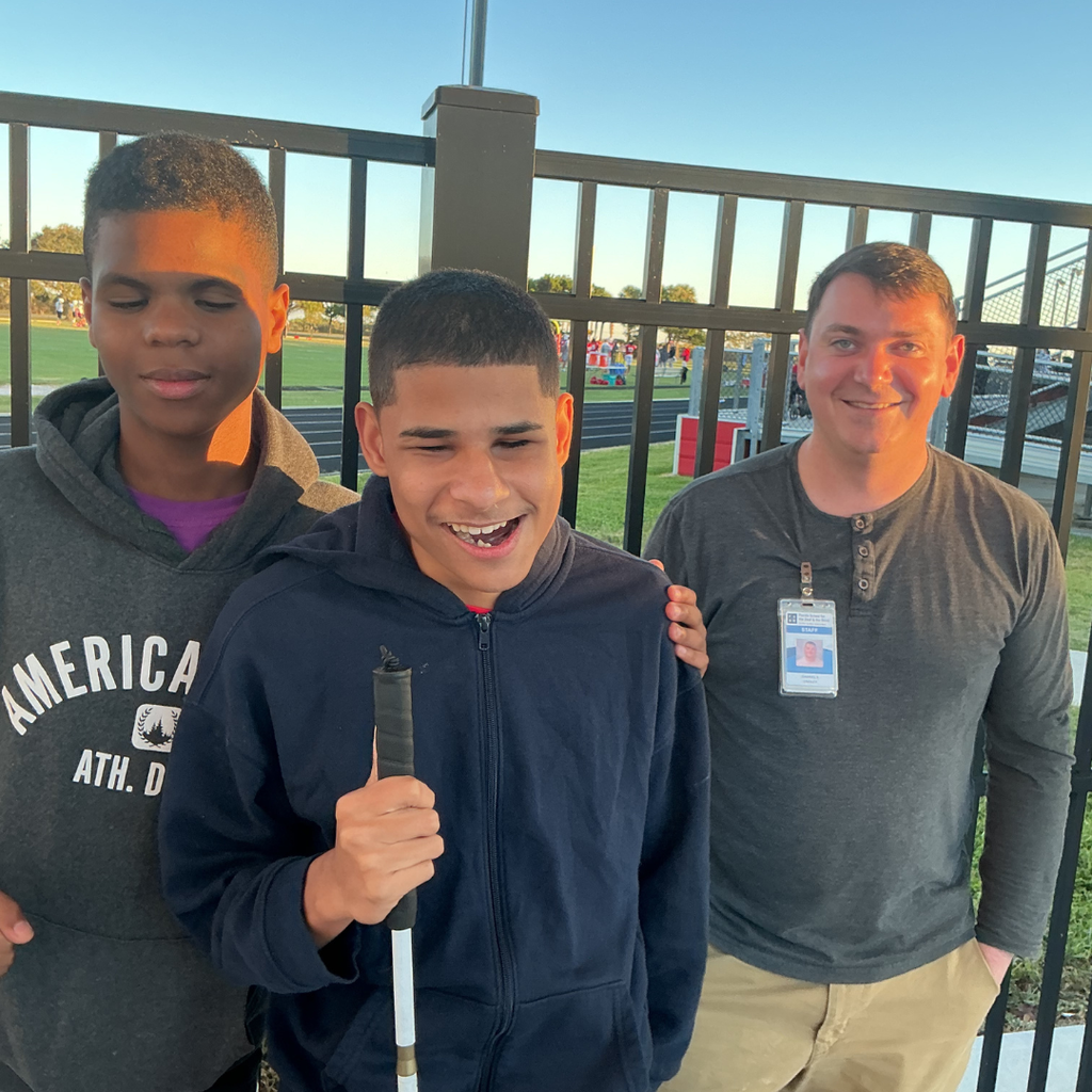 Two students and staff member smile outside as they are walking around the track. 
