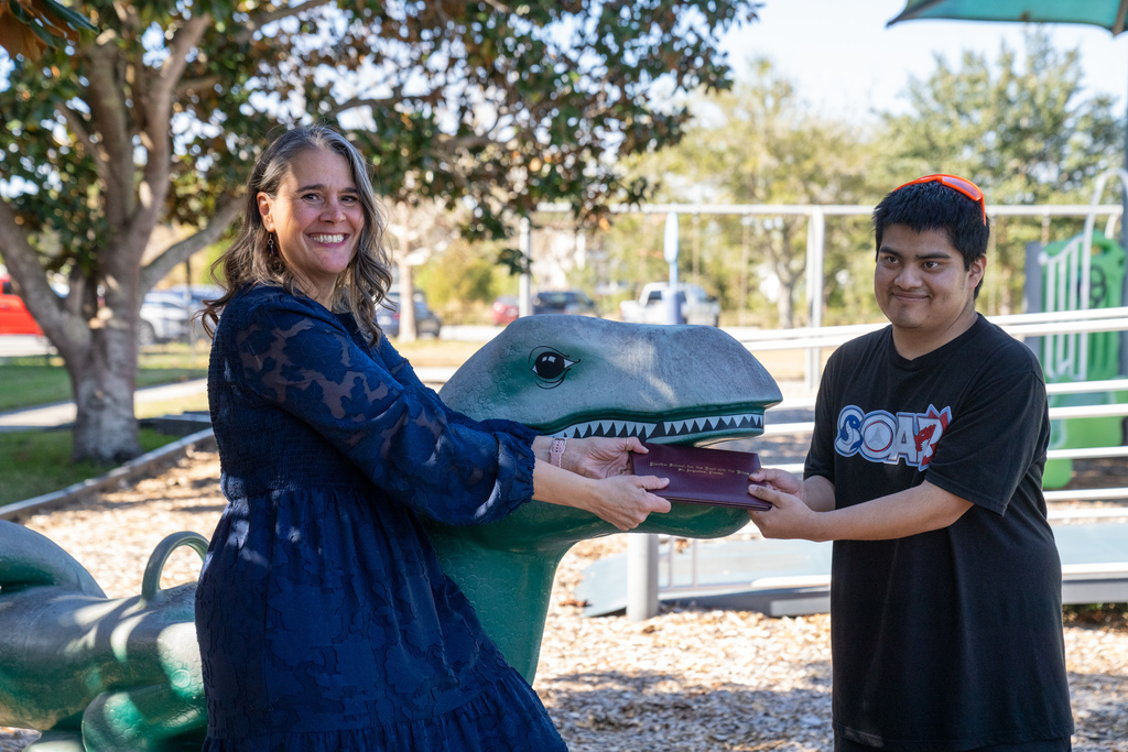 Tracie Snow and Max hold his diploma with the dinosaur eating the diploma outside on Kramer playground. 