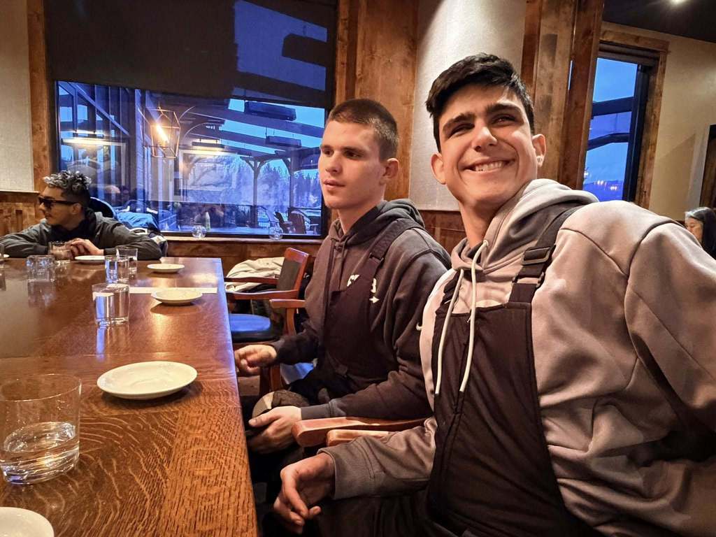 Two blind students smile together for a photo inside a restaurant waiting on their food. 
