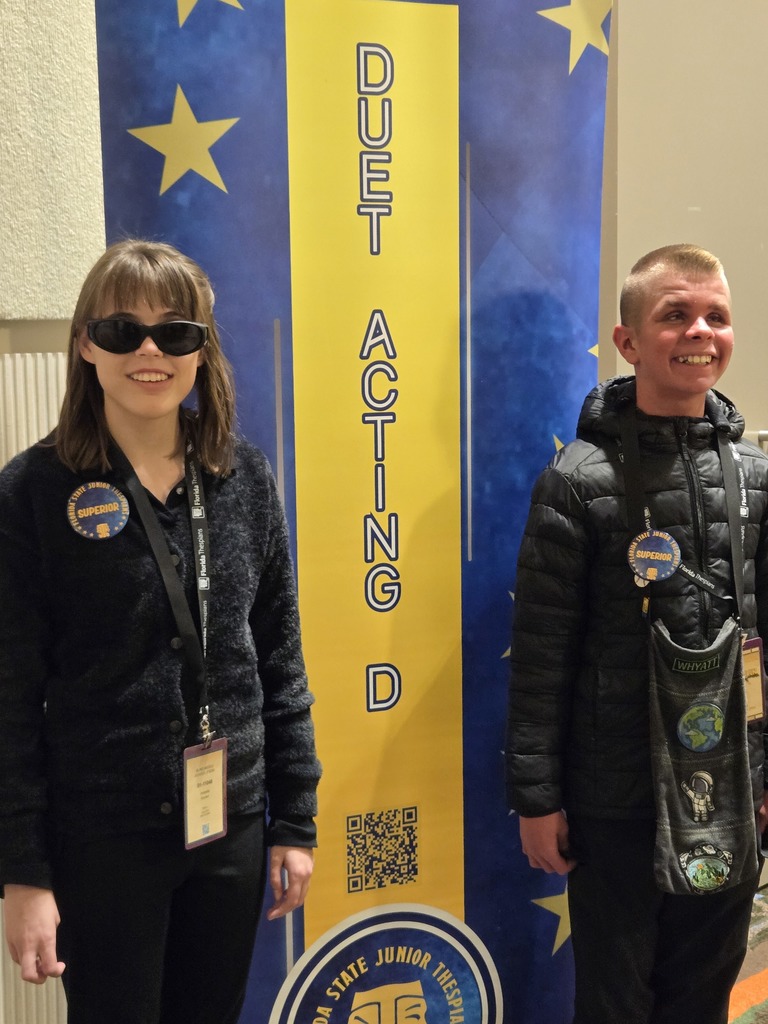 Arabella and Whyatt in front of the sign to their competition room. they are wearing their Superior buttons