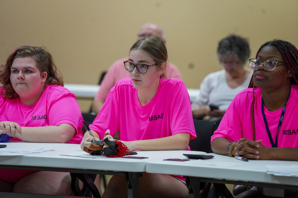 A student wearing a pink shirt looking at the board thinking about her answer.
