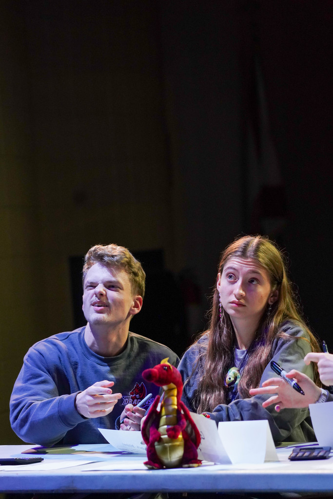 Two students look at the board and think hard at the table on stage in Kirk.