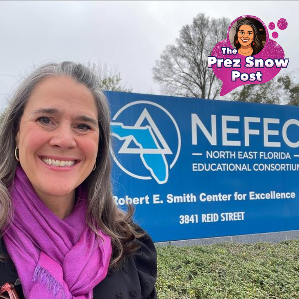 President Snow is wearing a bright magenta scarf and a smile as she stands in front of a large blue sign for the North East Florida Educational Consortium (NEFEC) at the Robert E. Smith Center for Excellence. Trees and a parked car appear in the background.