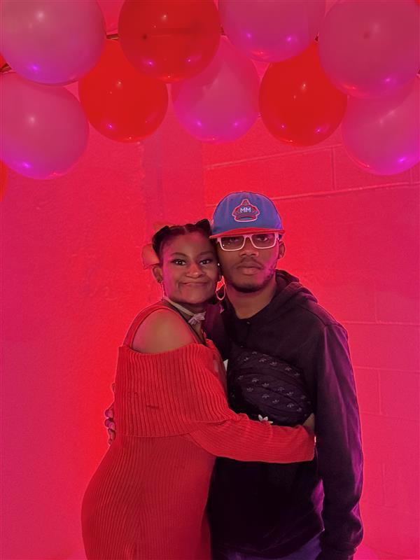 A couple smile together in front of a red valentine day backdrop.