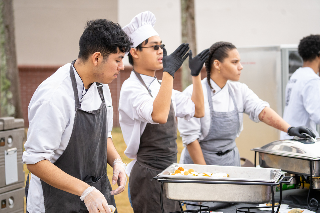 Culinary Art students dressed in chef hat and apron show off their talents outside.