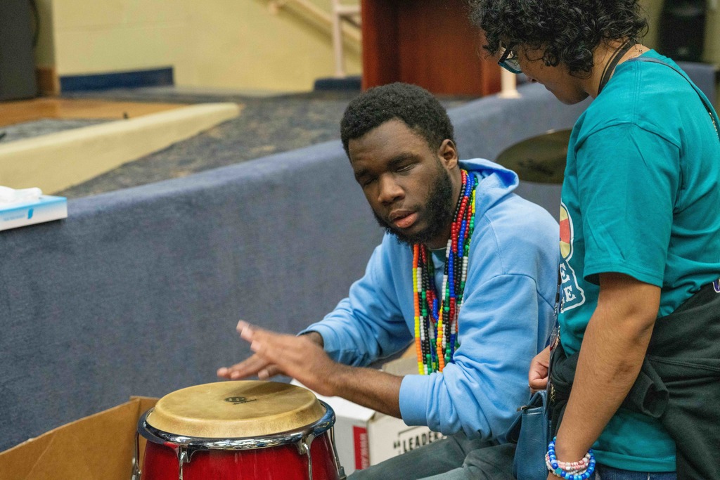 A student is participating in the drum circle inside the music building. 