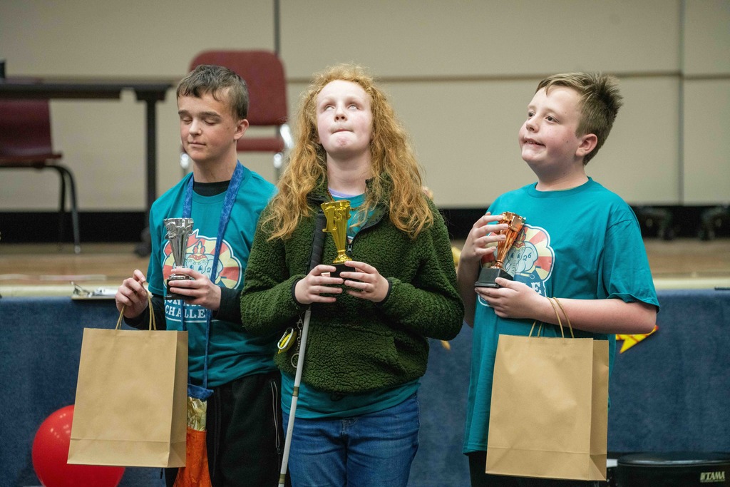 Three students hold their trophies and smile for a photo inside the music building. 