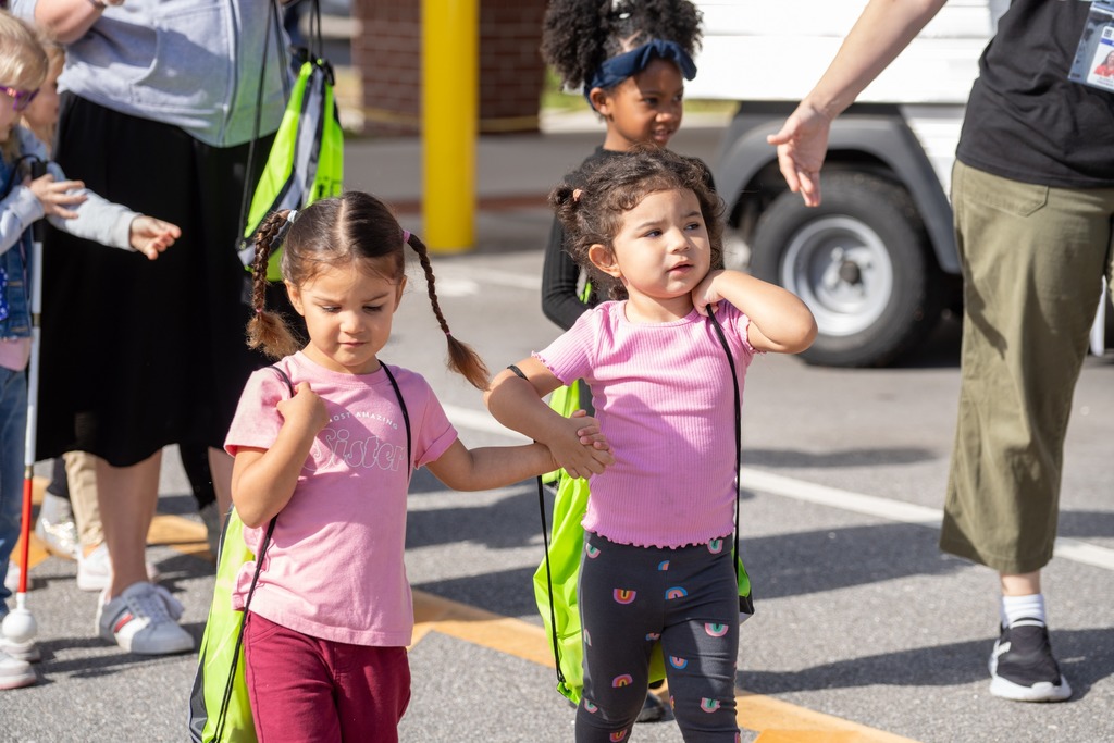Two ELC students hold hands walking outside around the safety far event. 