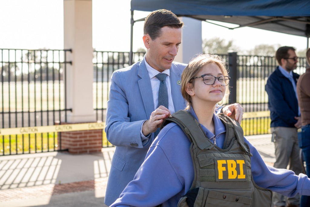 A FBI helps a student put on a FBI vest outside. 