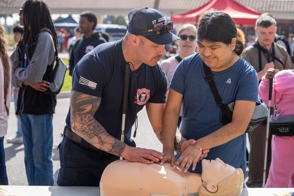 A student learns how to do CPR taught by a Fire Rescue worker outside. 