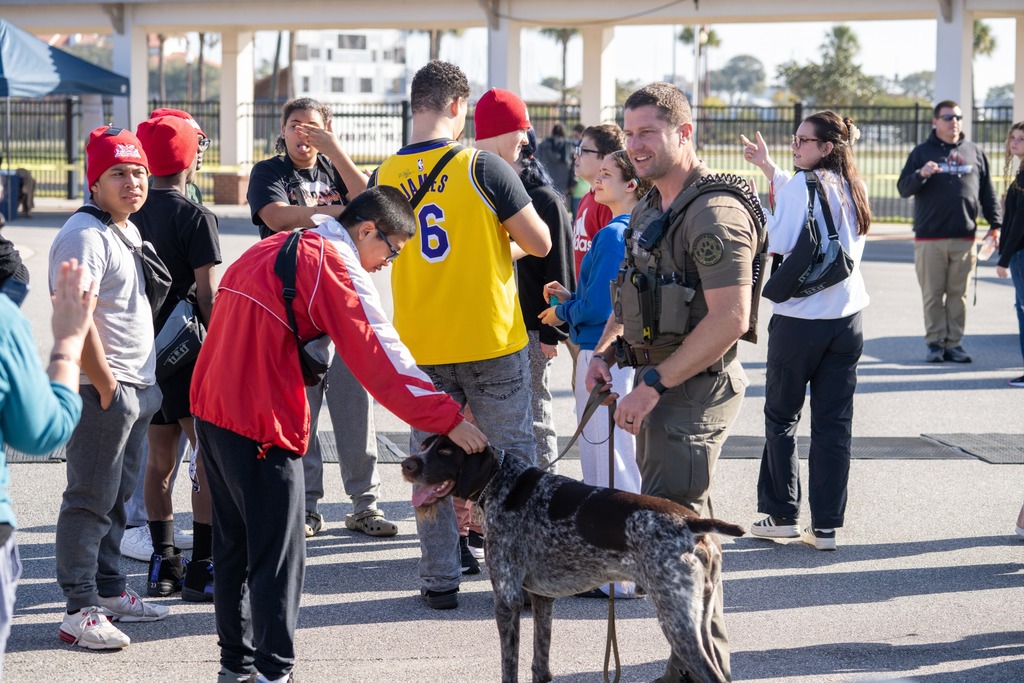 A police officer with a dog allows a student to pet the dog outside. 